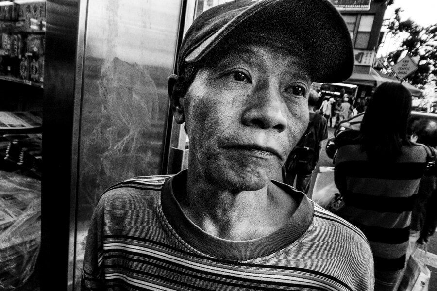 Close black and white street portrait of an older man in a cap looking at the camera