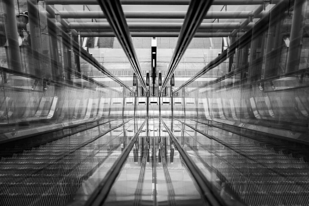 Black and white photo of escalators whose lines converge toward the center of the frame
