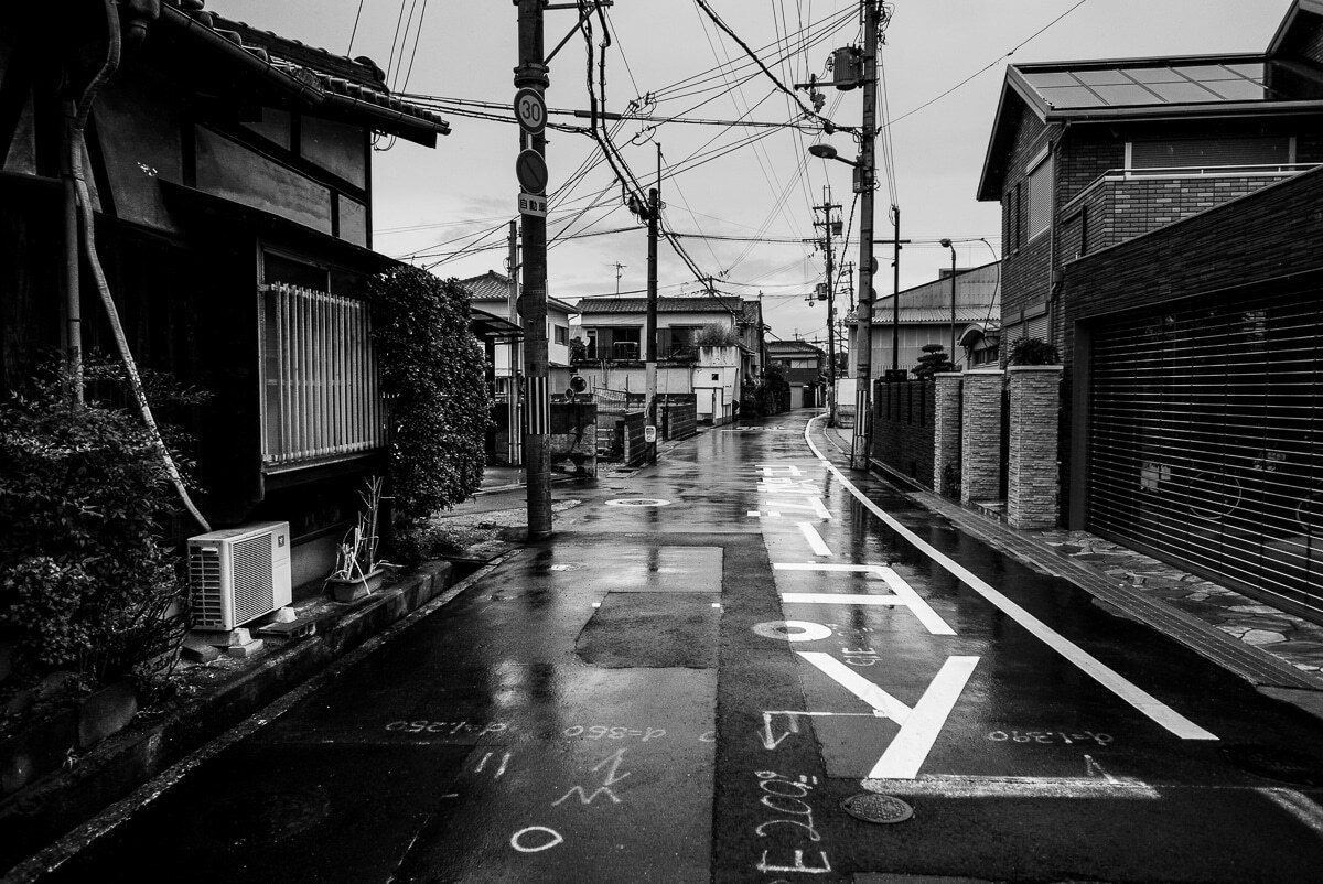 An empty narrow residential street after rain with power lines overhead
