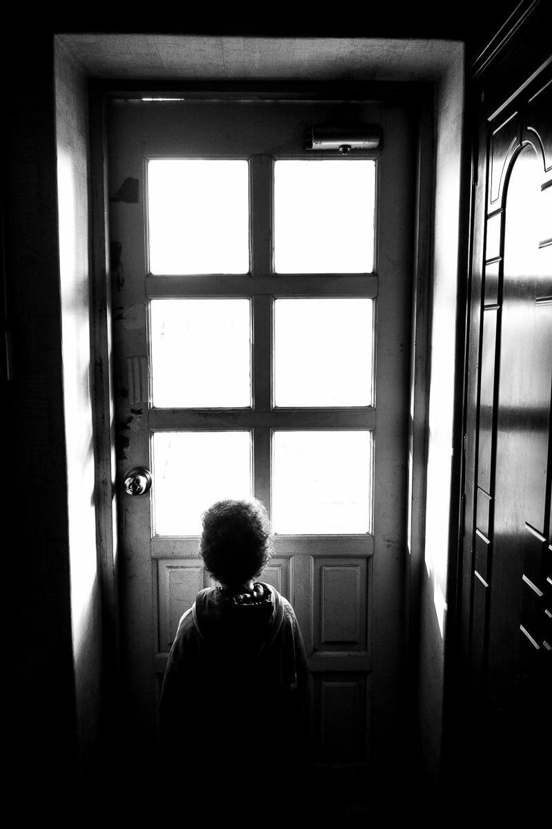 Silhouette of a small child standing at a glass door with bright light behind