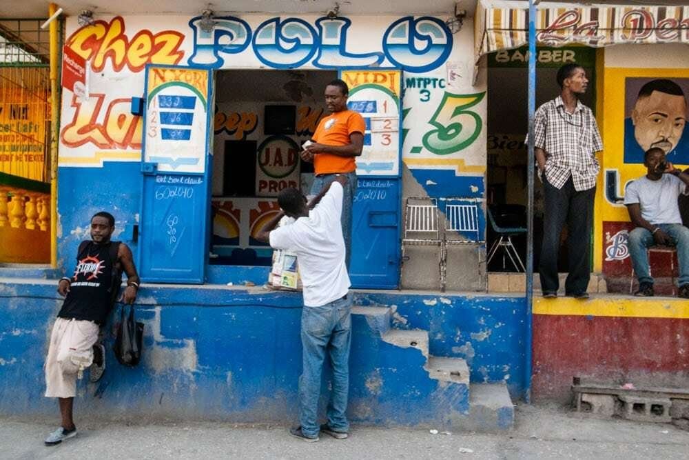 Colorful Haitian storefront painted blue and yellow with men standing and leaning in front of it