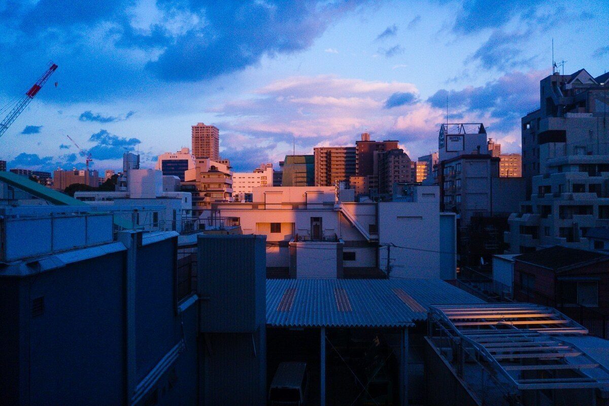 City rooftops at dusk with pink light on the buildings under a blue sky