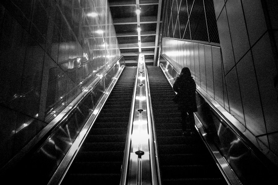 Black and white photo of escalators with strong converging lines and a lone figure on the right
