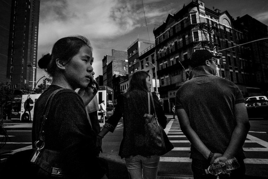 Pedestrians waiting at a Manhattan crosswalk under buildings, black and white street photography
